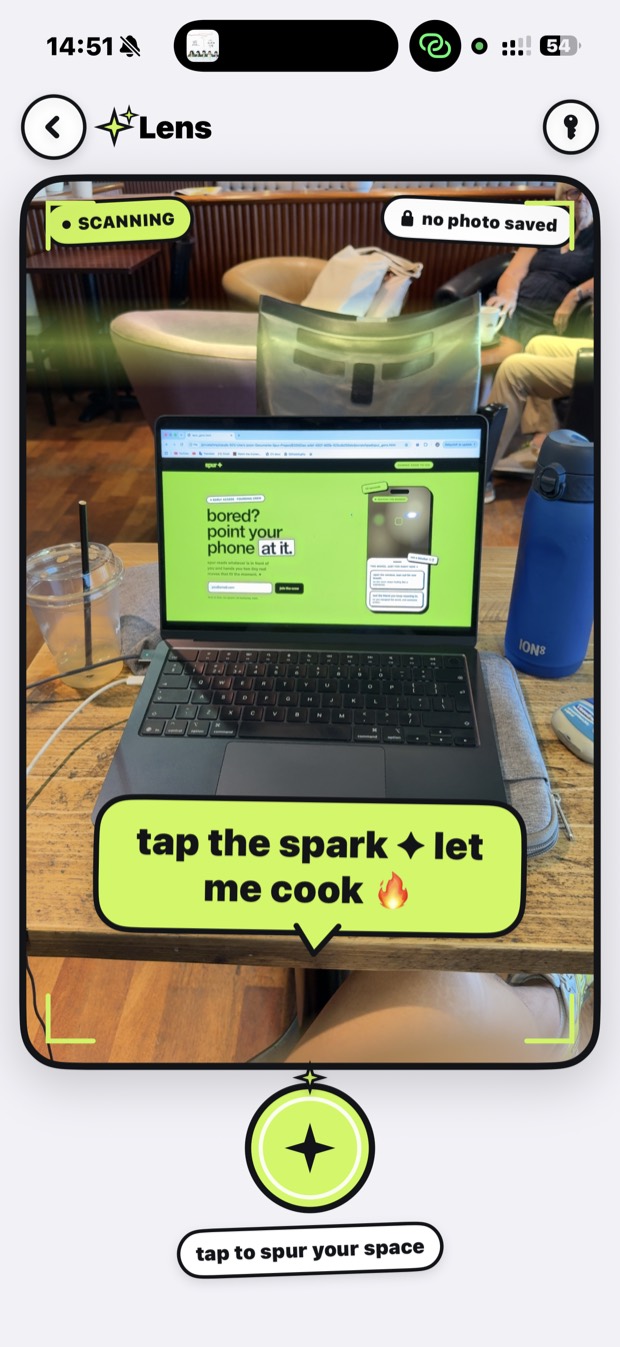 spur's Lens screen looking at a real cafe table with a laptop and a drink, prompting you to tap the spark